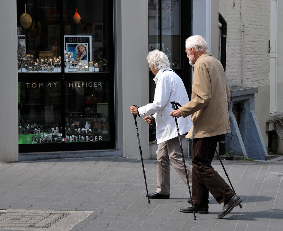 Zwei ältere Personen in der Stadt, die Trekkingstöcke als Gehhilfen benutzen.